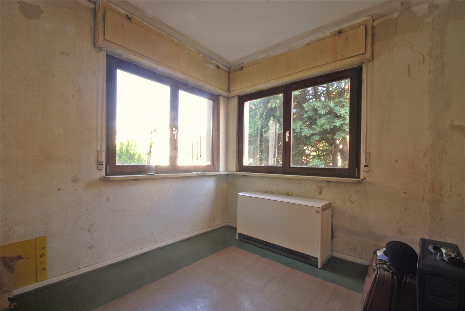 Wohnzimmer im Erdgeschoss. Für das Baujahr untypisch die sehr schön über-eck angelegten Fenster. Die Nachtspeicheröfen enthalten kein Asbest. In der gesamten Wohnung des Erdgeschosses wurde bereits ihre zukünftige Renovierung vorbereitet. - Oliver Reifferscheid - Immobilienmakler Darmstadt
