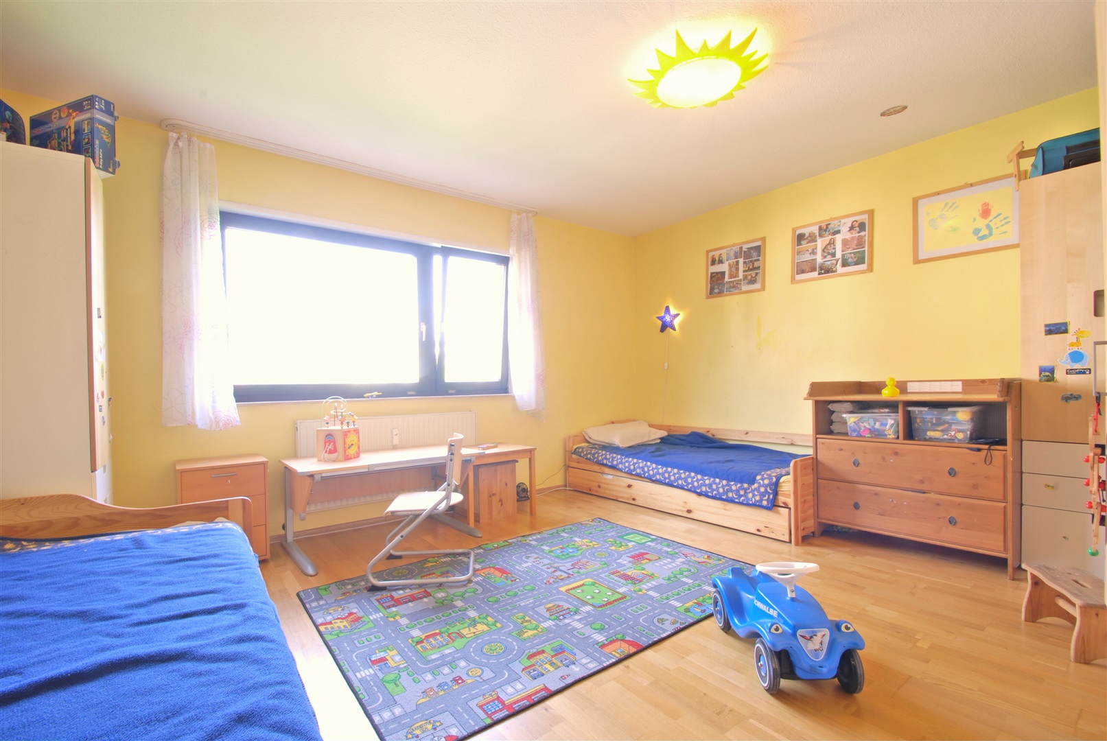 Helles Kinderzimmer mit warmen Eichenfertigparkett. Das Fenster im Hintergrund verfügt über einen manuellen Rollladen - Oliver Reifferscheid - Immobilienmakler Darmstadt