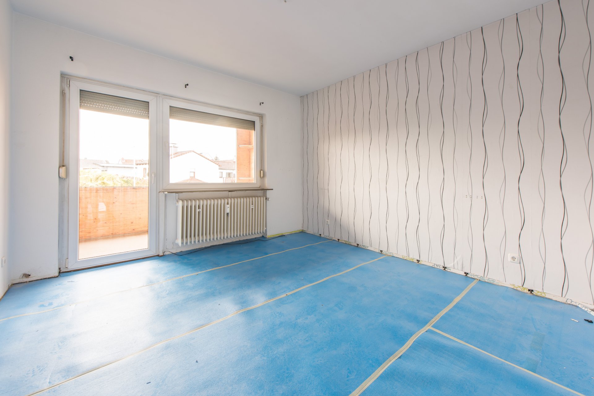 Schlafzimmer mit Zugang zum teilüberdachten Balkon auf der Gartenseite. Der blaue Untergrund ist die alte Trittschalldämmung - Oliver Reifferscheid - Immobilienmakler Darmstadt